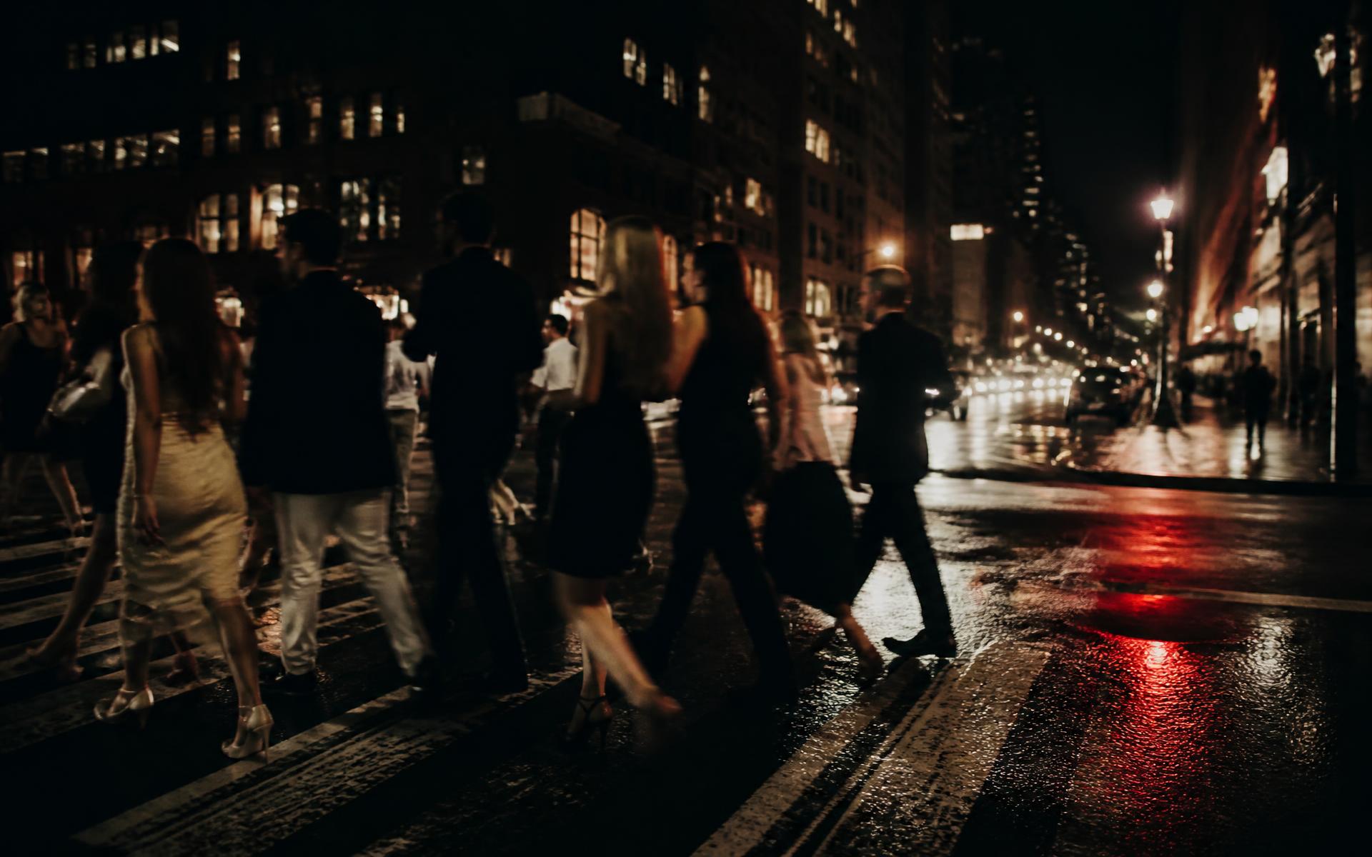 People crossing a New York street at night under warm streetlight